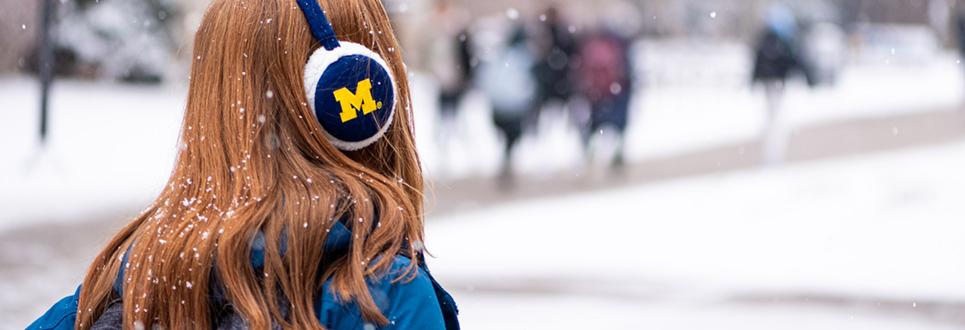 Student outside in the snow wearing earmuffs with M logo